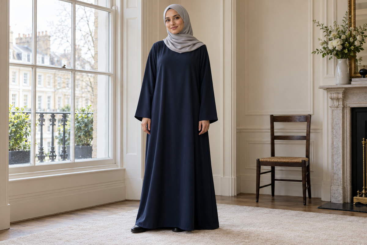 Model in a relaxed navy abaya and pale grey hijab beside a townhouse window